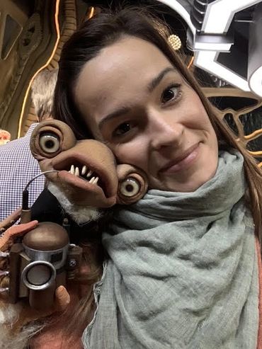 A woman poses with a quirky puppet with large eyes and sharp teeth.