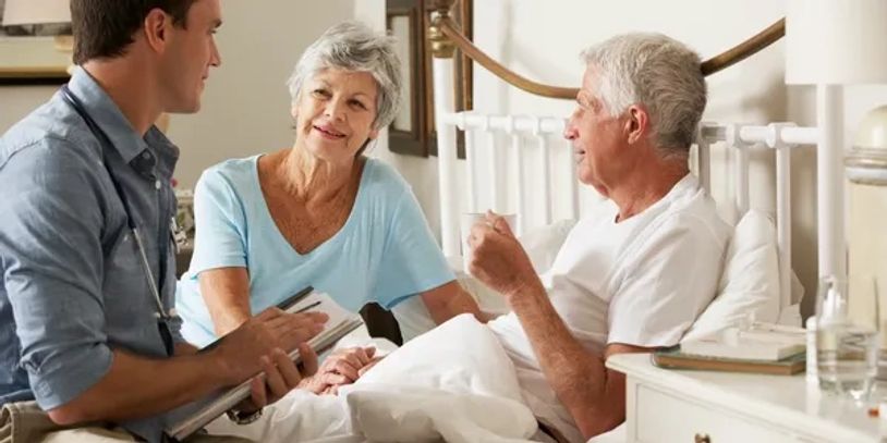 Doctor discussing with elderly couple in a bedroom.
