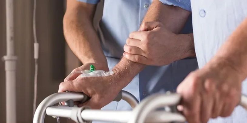 Person helping another using a walker with an IV in place.