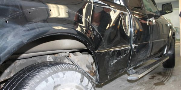 Black vehicle with visible dents and scratches on the side panel and door.