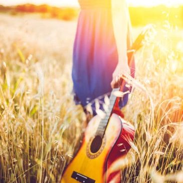 Person holding a guitar in a sunlit wheat field.