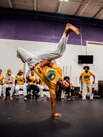 Man performing an impressive one-handed capoeira move indoors.