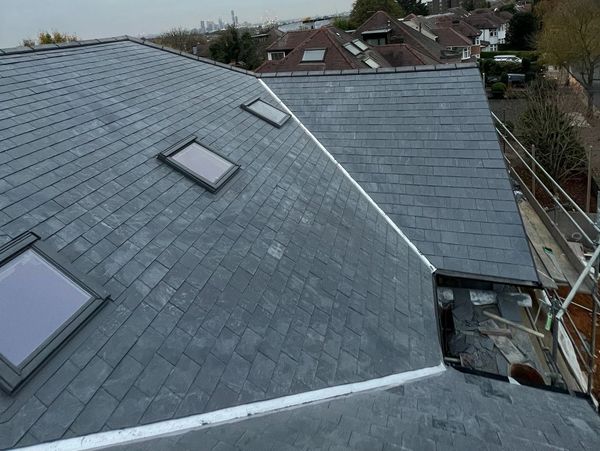 Newly installed dark grey slate roofs with skylights in a suburban neighborhood on an overcast day.