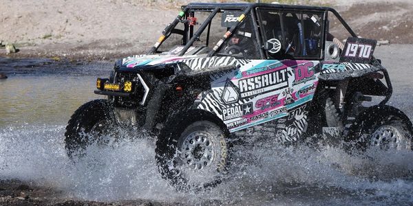 Off-road racing vehicle splashing through water during a race.