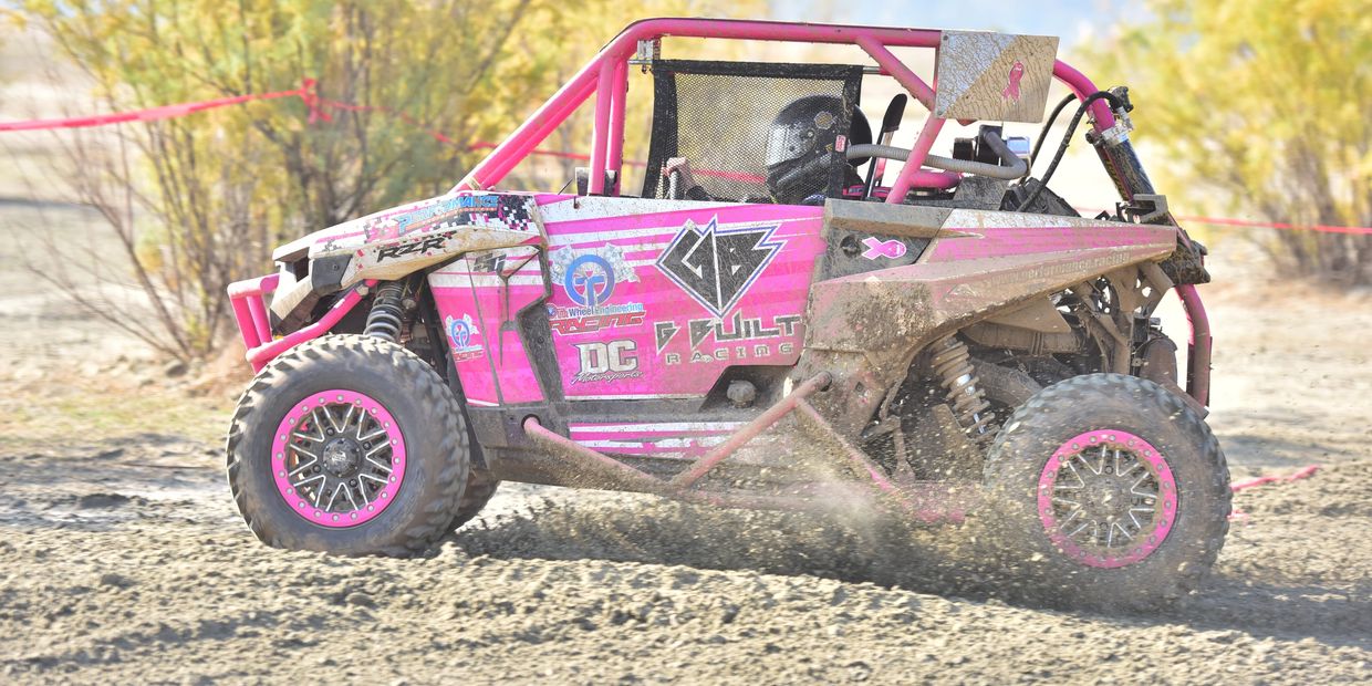 Pink off-road racing buggy kicking up dirt on a sandy trail.