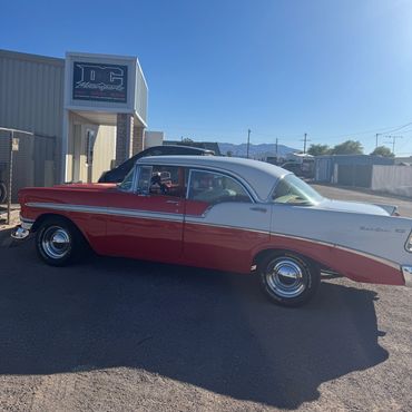Classic red and white vintage car parked outside a shop under clear blue sky.