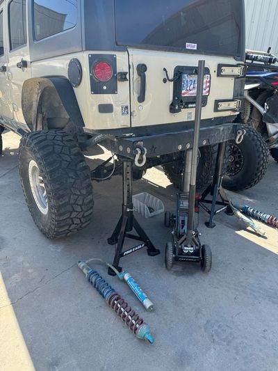 Jeep lifted on jack stands with removed suspension parts and floor jack.