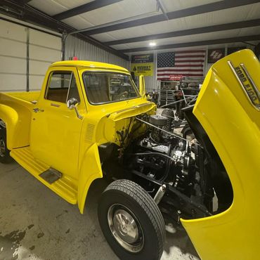 Classic yellow pickup truck with its hood open in a garage.