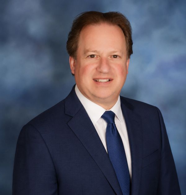 Professional man in navy suit and tie against a blurred blue background.