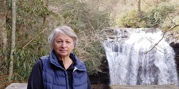 Woman standing near a waterfall surrounded by nature.