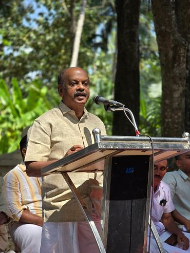Man speaking at an outdoor event with microphone and audience.