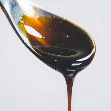 Cuchara con miel oscura y espesa goteando.