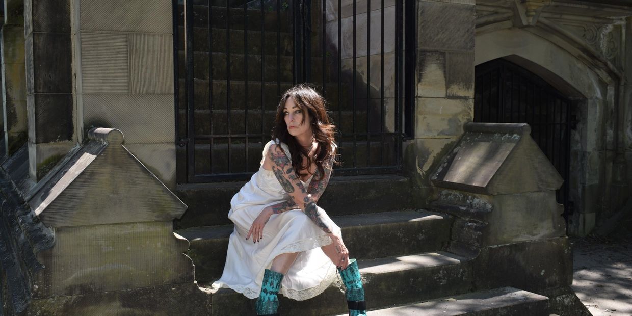 woman i a white slip and high fashion boots sitting on stairs at a cemetery 