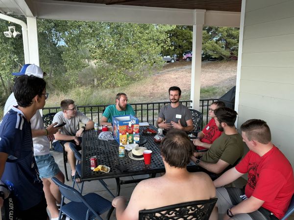 Group of friends chatting on a porch around a table with snacks.