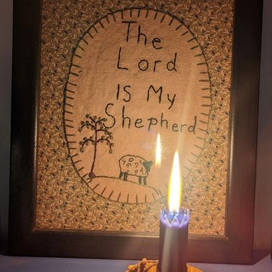 Framed embroidery with 'The Lord is My Shepherd' and a lit candle in front.