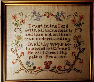 Embroidered biblical verse surrounded by colorful flowers and birds in a wooden frame.
