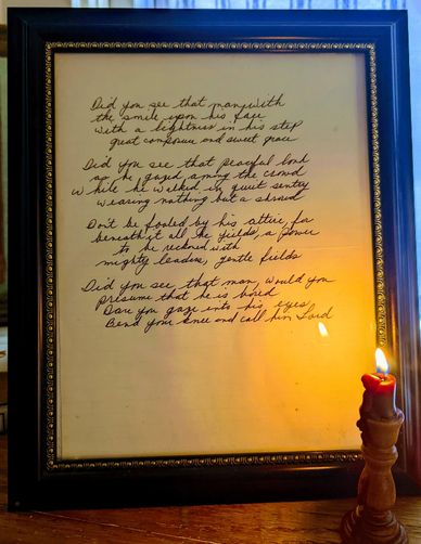 Framed handwritten poem illuminated by a lit candle on a wooden surface.