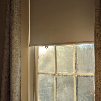 Sunlight filters through a partially covered window with patterned curtains.