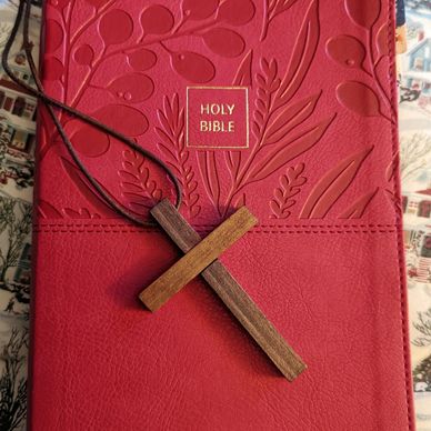 Red Holy Bible with embossed floral design and wooden cross necklace.