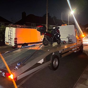 A motorbike with learner plates on a flatbed truck at night.
