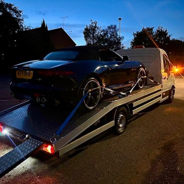 Sports car loaded on a flatbed tow truck at dusk.