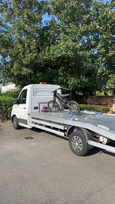 Flatbed truck carrying a dirt bike outdoors.