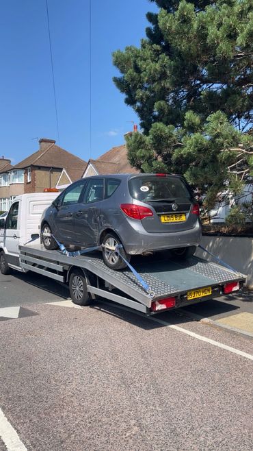 Gray car strapped on a flatbed tow truck on a residential street.