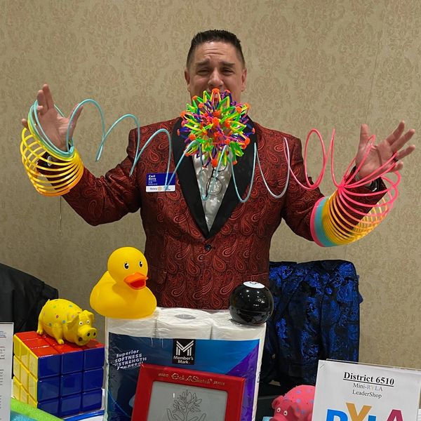 Man in a red jacket holding colorful slinkies with various toys and items on the table.