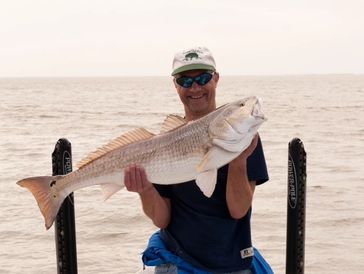 Man proudly holding a large fish on a boat.