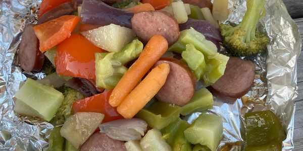 Grilled sausage with mixed vegetables on foil.