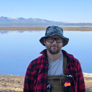 Noam with hat and bear spray in front of mountains and lakes