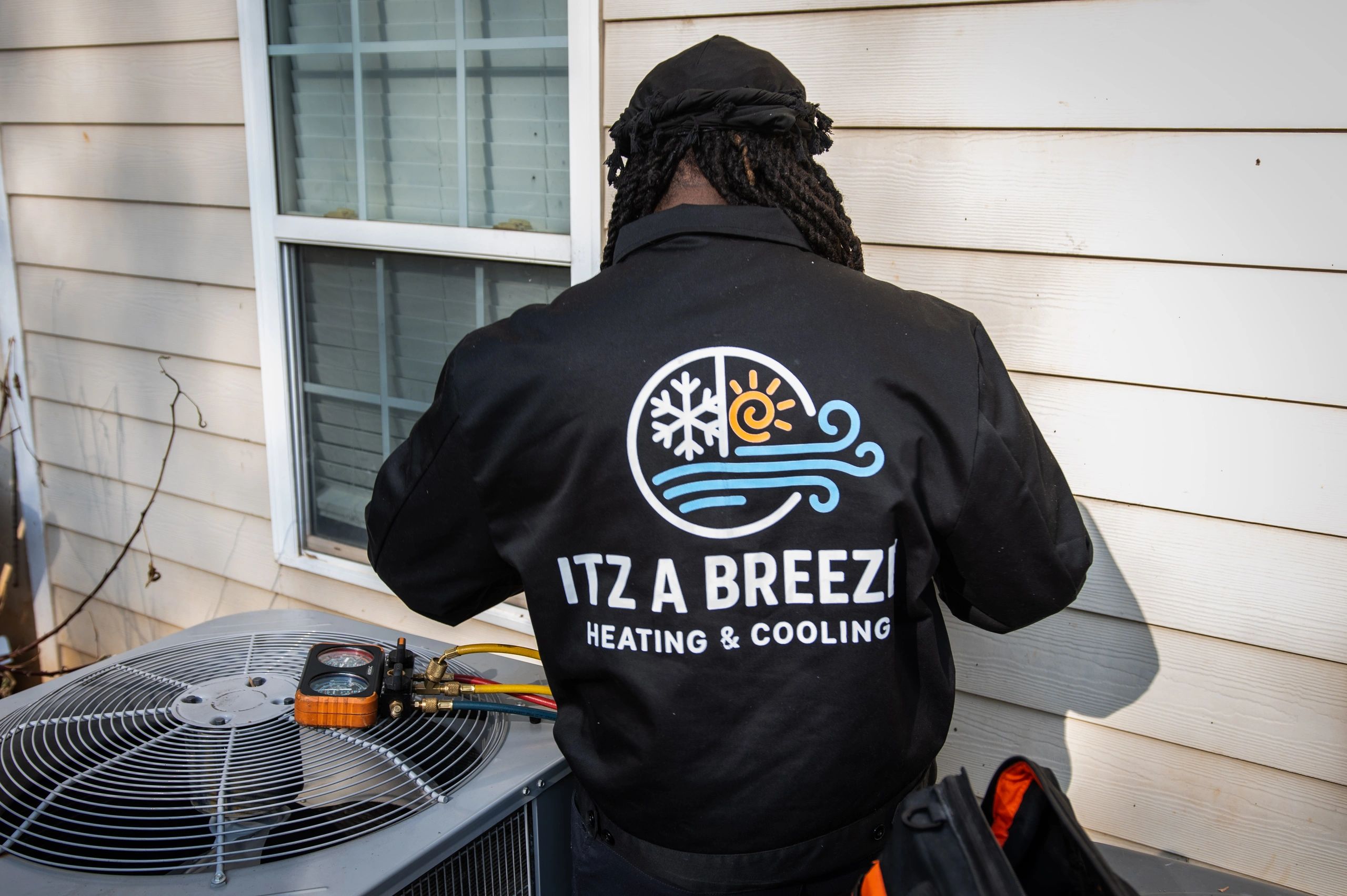 Technician from Itz A Breezi Heating &amp; Cooling servicing an outdoor HVAC unit.