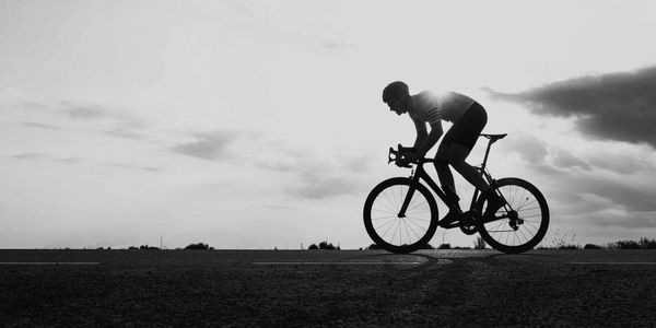 Silhouette of a cyclist riding against a cloudy sky at sunset.