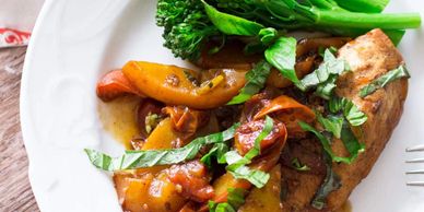 Grilled chicken breast with sautéed bell peppers and steamed broccolini on a white plate.