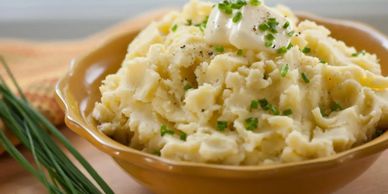 Creamy mashed potatoes topped with butter and chives in a brown bowl.