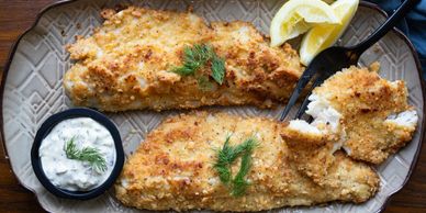 Golden breaded fish fillets with lemon wedges and creamy dill sauce.