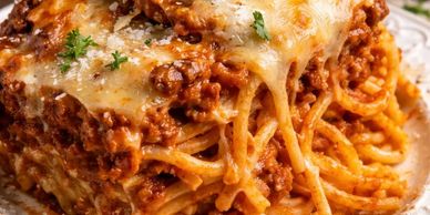 Close-up of cheesy spaghetti with meat sauce and parsley garnish.