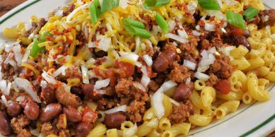 A plate of chili mac topped with cheese, onions, and green onions.