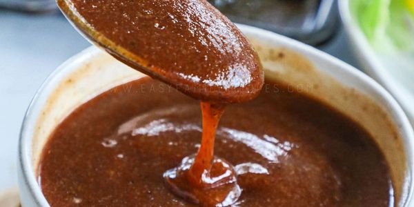 Thick, rich brown sauce being poured from a spoon into a white bowl.