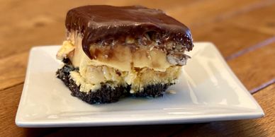 A layered dessert bar with chocolate, cream, and cookie crust on a white plate.