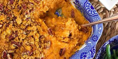 A baked sweet potato casserole with a crunchy pecan topping in a decorative blue dish.