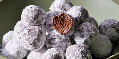 Chocolate truffles dusted with powdered sugar, one with a bite revealing a rich chocolate center.