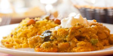 Close-up of a plate with yellow rice and vegetable curry topped with cream.