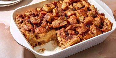 A baked bread pudding dessert in a white dish with a portion removed.