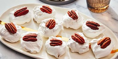 Meringue cookies topped with pecan halves on a white plate.