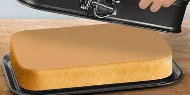 A freshly baked rectangular cake being removed from a springform pan.