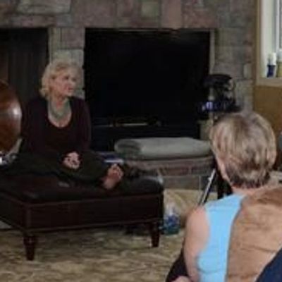 Group of people gathered in a cozy living room with a stone fireplace.