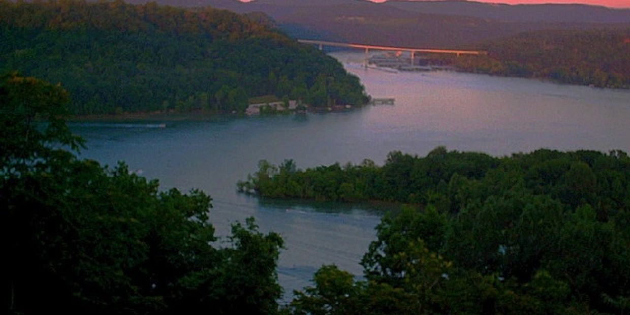 A river winding through lush green hills at dusk with a distant bridge.