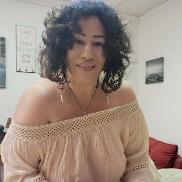 Woman smiling in an off-shoulder beige top.