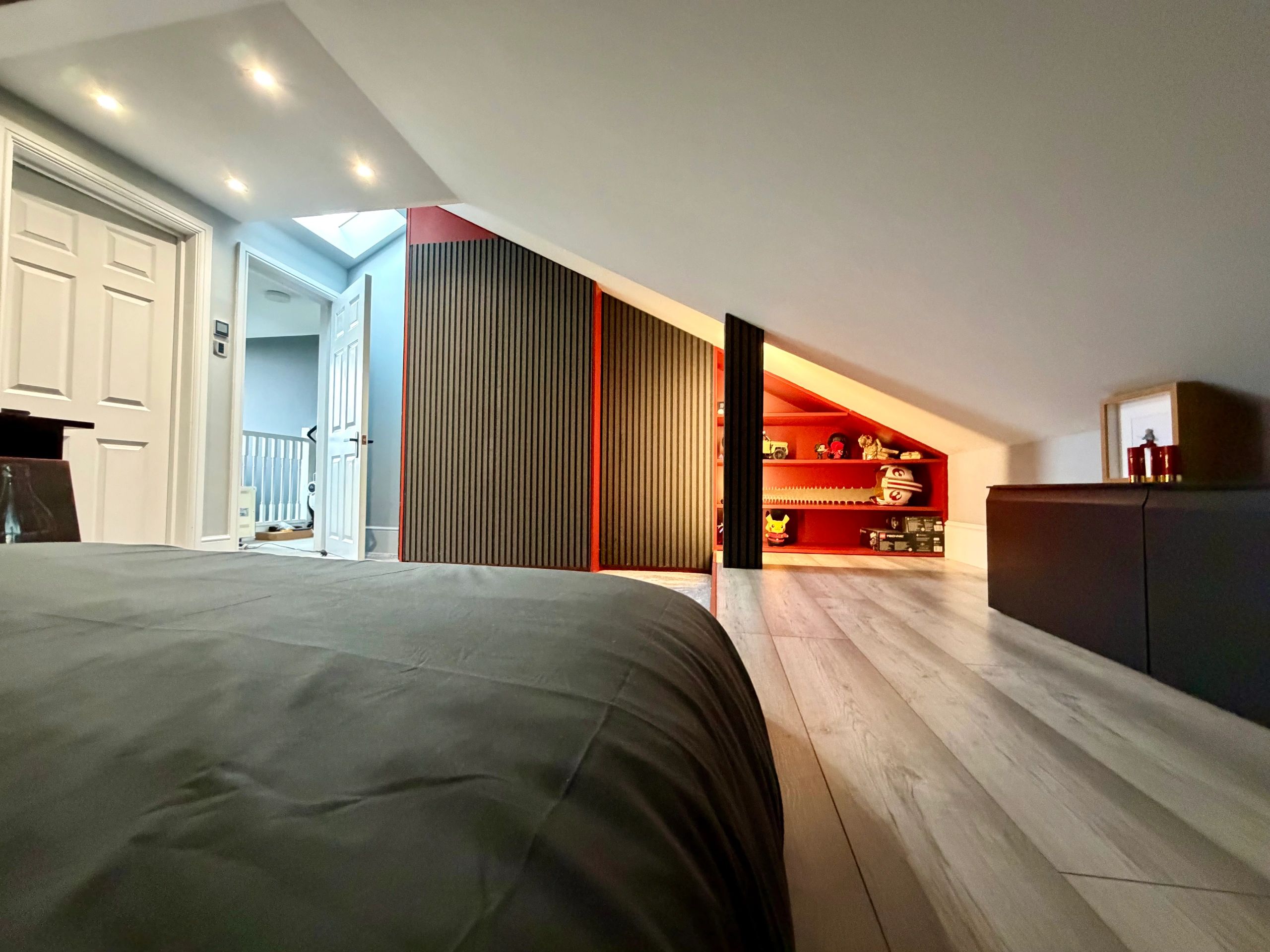 Modern attic bedroom with slanted ceiling and built-in red shelves.